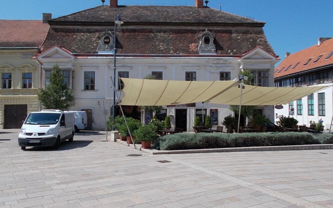 Grande cobertura de lona clara sobre o terraço de um restaurante em frente a um prédio histórico
